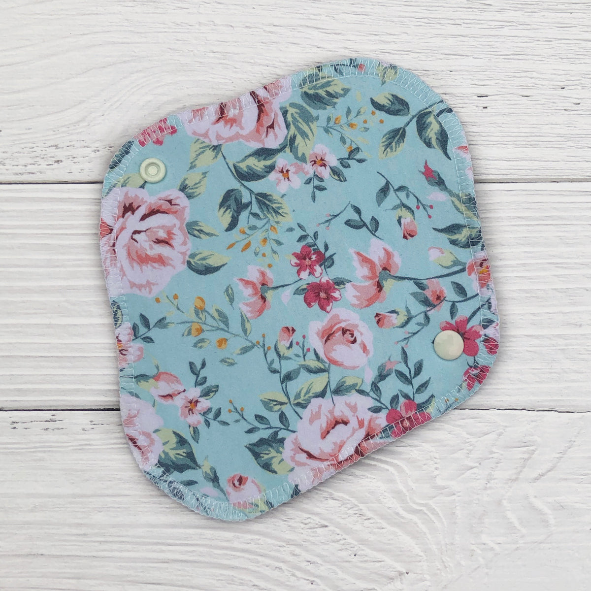 reusable pantyliner in a mint floral print on a white wood background