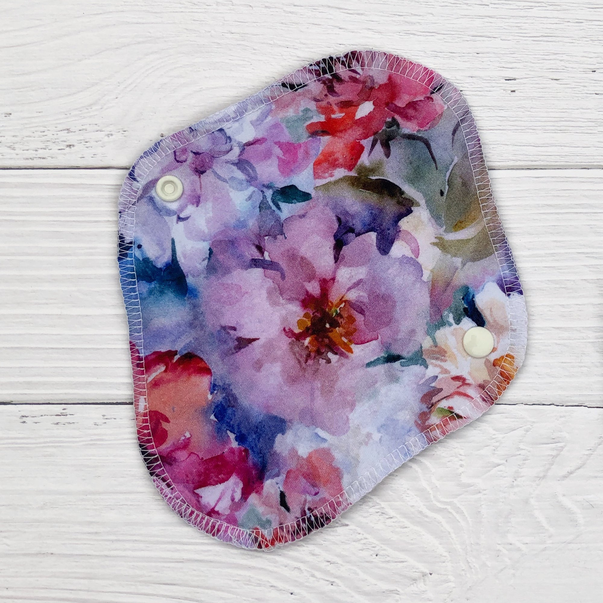 reusable pantyliner in a watercolour peony print on a white wood background